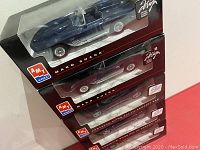 Stack of five boxed die cast cars: two AMT/Ertl Mako Shark models in blue and three AMT/Ertl Chevrolet Corvette Sting Ray III Concept Car models in maroon. Packaging shows signs of wear and damage.
