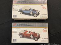 Photo of two boxes with Scale Models die cast metal model kits. One box labeled Packard Victoria with blue car image, the other Packard Phaeton with red car image. Boxes show wear and damage.