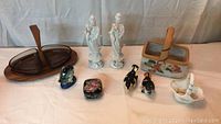 Various assorted decorative items including wooden trays, porcelain figurines, ceramic birds, trinket box, and basket spread on a table.