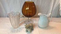 Overview of all four items: amber glass vase, white ceramic pitcher, clear glass pitcher, elephant figurine