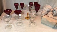 Photo of assorted red and clear stemware glasses with some gold rims and amber stemmed glass on a white surface.