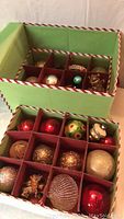 Overview of two green storage totes containing multiple vintage Christmas glass and plastic ball ornaments separated by cardboard dividers.
