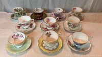 Top view of the 9 tea cups with matching floral saucers arranged in 3 rows on a white cloth backdrop.