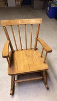Front view of the antique wooden child rocking chair showing the vertical spindle backrest, armrests, and flat seat.