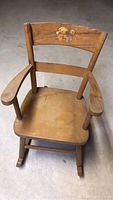 Full view of antique child's wooden rocking chair showing seat, armrests, backrest with painted decoration.