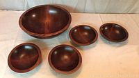 Photo showing set of five wooden bowls: one large bowl and four smaller matching bowls, all smooth finished with natural wood grain.