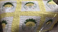 Close-up view of the quilt's floral appliqué design with yellow flower and green leaves, showing detailed hand stitching and quilting pattern.
