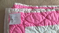 Quilt folded showing pink-and-white border and handwritten note indicating size and hand quilting