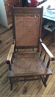 Front view of the antique rocking chair showing cane woven seat and back with wooden armrests and base rockers.