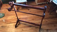 Front view of a wooden quilt rack showing two horizontal bars and turned legs with stabilizing feet on a hardwood floor.