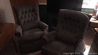 Photo showing two tufted recliners with armrests and seating cushions in a dark olive/brown-green fabric upholstery with some wear on piping edges.