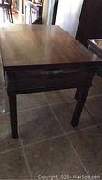 Wooden end table showing tabletop surface and drawer front with plastic wrap on legs.