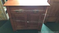 Front view of antique wooden washstand showing drawer with two handles and double-door cabinet with a single round knob, wood grain visible.