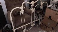 Photo of iron headboard showing decorative scroll and floral metal design, cream color finish