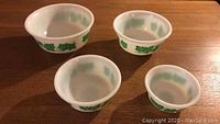 Set of four vintage milk glass mixing bowls with green leaf pattern arranged together on wooden surface showing variety of sizes from 5 to 8 inches width.