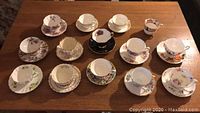 Full set of thirteen tea cups with saucers and one extra tea cup without saucer arranged on wooden table.