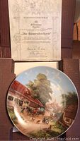 Collector plate front with rural German village scene in original packaging alongside certificate of authenticity