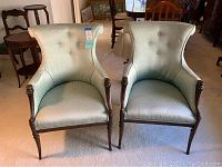 Front view of two vintage parlor chairs with light blue dotted upholstery, button tufted backs, carved claw feet