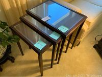 Set of three wooden nesting tables with glass inset tops stacked together showing size difference.