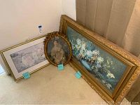 Photo showing all three framed artworks positioned on carpeted floor against corner walls for size and condition reference.
