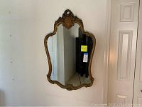 Full view of the vintage ornate framed wall mirror hanging on a white wall, showing its overall shape and frame details.