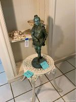 Garden statue of man in historical attire standing on wrought iron plant stand with decorative design