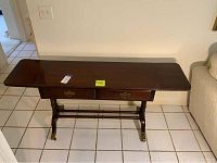 Front angle view of vintage wooden desk with drop leaf ends extended, showing two drawers and caster wheels on legs.