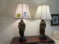 Pair of vintage figural table lamps each approximately 35 inches tall with white fabric shades on wooden table.