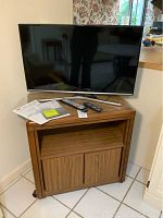 Samsung LED TV on wooden TV cart with two remotes and user manual on top.