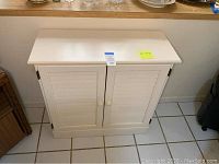 White wood storage cabinet closed showing two doors with knobs and flat top surfaces.