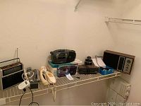 Overview of items on shelf: Panasonic FM-AM radio, portable cassette player on box, Samsung flip phone in box with charger, Panasonic cordless phone and wall handset.