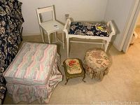 All items in the lot arranged on the floor: white wooden chair, upholstered bench with floral cushion, two small foot stools including one embroidered and one round with ruffled skirt, and one large rectangular fabric-covered footstool.