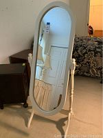 Full view of oval mirror with white wooden frame and stand in bedroom setting