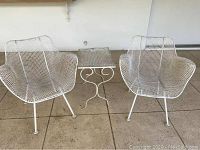 Overview of two chairs and side table on patio floor against white wall