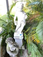 Photo showing both statues together on patio surrounded by plants.
