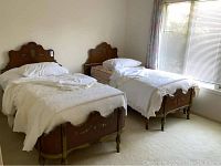Full image showing two antique twin beds with white bedding, placed side by side on carpet under window with curtains