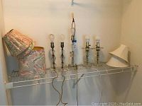 Overview of all lamps and lampshades on wire shelf, showing the two pairs and single lamp with clear bases, metal components and fabric floral lampshades.
