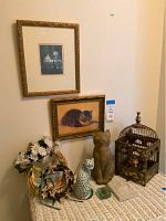 Wide shot showing the variety of kitty-themed decor items including cat figurines, framed cat art, wreaths, and bird cage on wicker table.