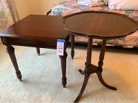Two vintage wooden side tables in a bedroom setting on carpet; one square Bombay table with turned legs, one round pedestal table with claw feet