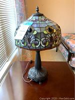 Side view of Tiffany style lamp showing multicolored stained glass shade and metal base with power cord on table.