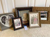 Set of four framed art prints and one ornate gold framed mirror on beige carpet against white paneled wall.