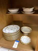 Shelved set of 12 Limoges porcelain dinner plates with floral and gold pattern, footed compote bowl, and small plate.