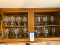 View of wooden display cabinet with 14 crystal goblets, 9 wine glasses, and 10 parfait bowls arranged on two shelves.