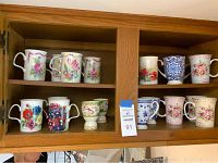 Two shelves of floral coffee cups, some identified as Roy Kirkman designs, and 2 Mintons egg cups.