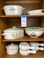 Shelf with Corning casserole with blue floral design, Shafford covered casserole with botanical design, Botanic Garden bowl, and cat. A lot tag