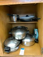 Set of stainless steel cookware with lids and handles inside cabinet showing various sized pots and saucepans.