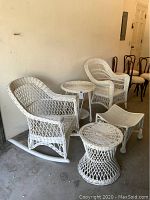 Photo showing the full set including rocking chair, armchair, two round tables, and the ottoman all in white wicker, with visible chipped and cracked paint.