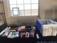Wide view of all painting supplies on black cloth including paint rollers, brushes, drop cloths, sponge applicators, and a tool set box.