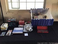 Full lot overview showing all items on black tablecloth under window including Makita sander box, red socket case, Toyota hub cap and blue storage bin with assorted items.