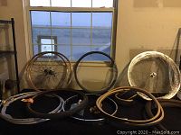 Multiple bicycle rims leaning against a wall and stacked on a table with loose tire casings and spokes